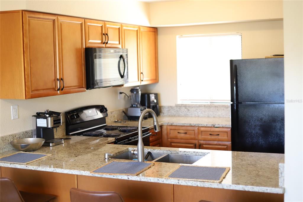 A kitchen features wood cabinets, granite countertops, a black refrigerator, and a stainless steel sink — 695 & 693 BELFLOWER PLACE, ALTAMONTE SPRINGS, FL