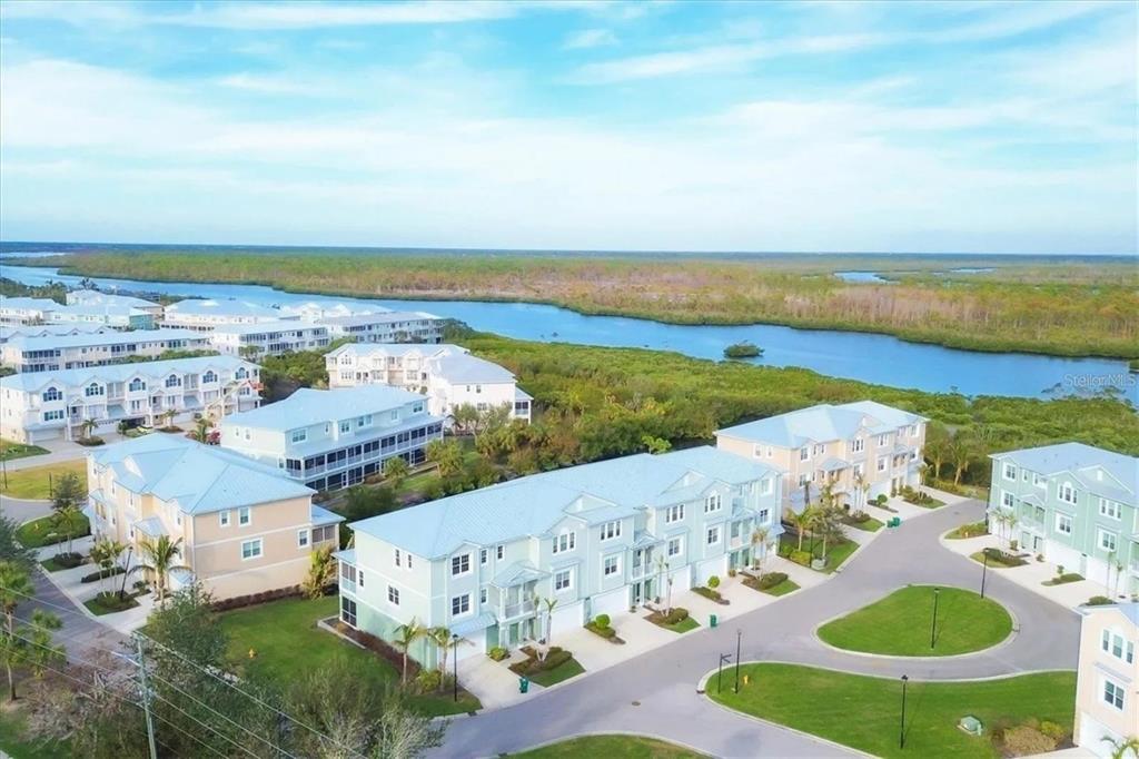 An aerial view shows several multi-story residential buildings with light-colored siding near a waterway — 10420 CORAL LANDINGS LANE UNIT 115, PLACIDA, FL