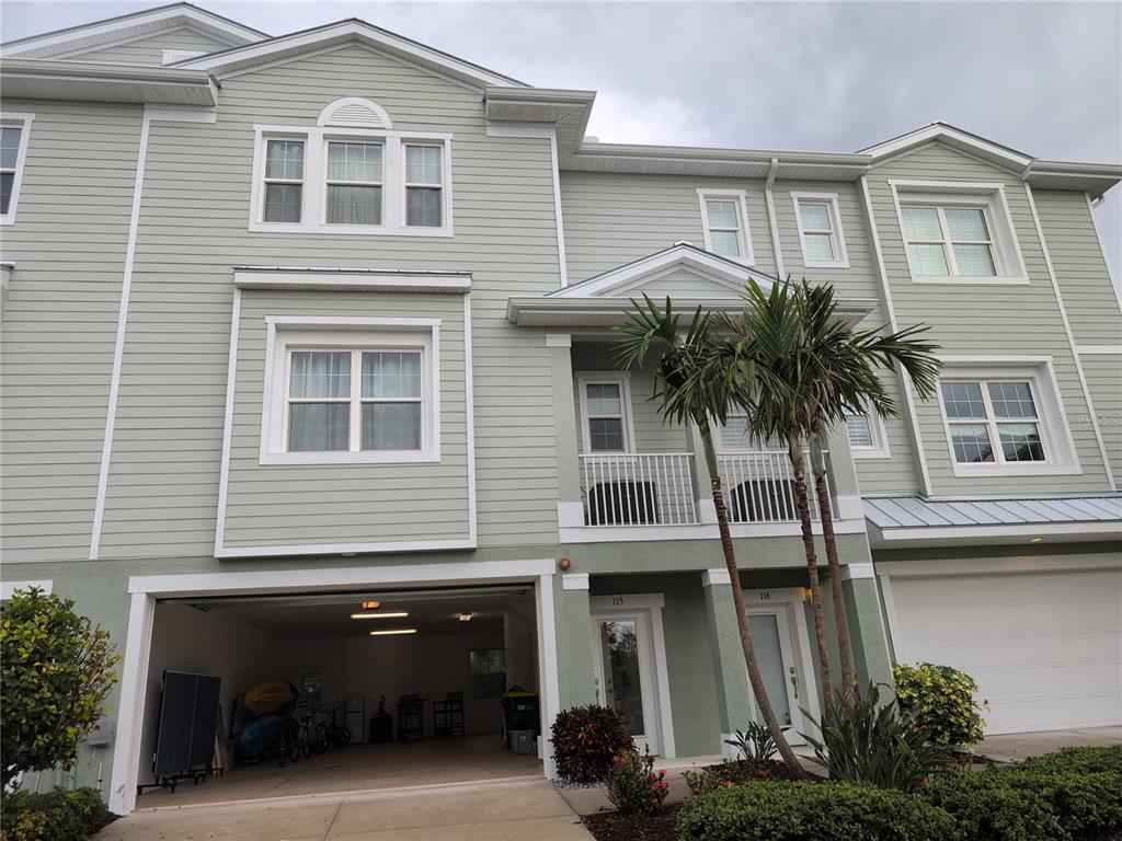A three-story townhouse exterior features light green siding, a ground-level garage, and a second-story balcony — 10420 CORAL LANDINGS LANE UNIT 115, PLACIDA, FL