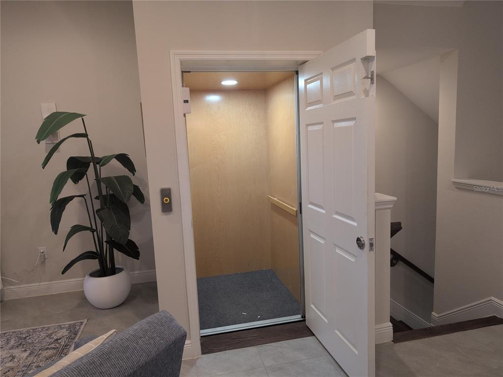 A residential elevator with light wood interior walls is positioned next to a staircase — 10420 CORAL LANDINGS LANE UNIT 115, PLACIDA, FL