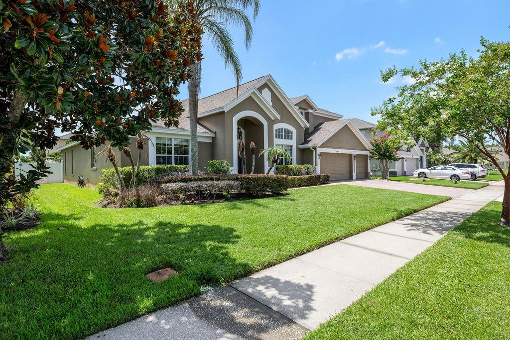 A tan suburban house with a two-car garage and a front lawn under a blue sky — 13624 LARSEN LANE, WINTER GARDEN, FL