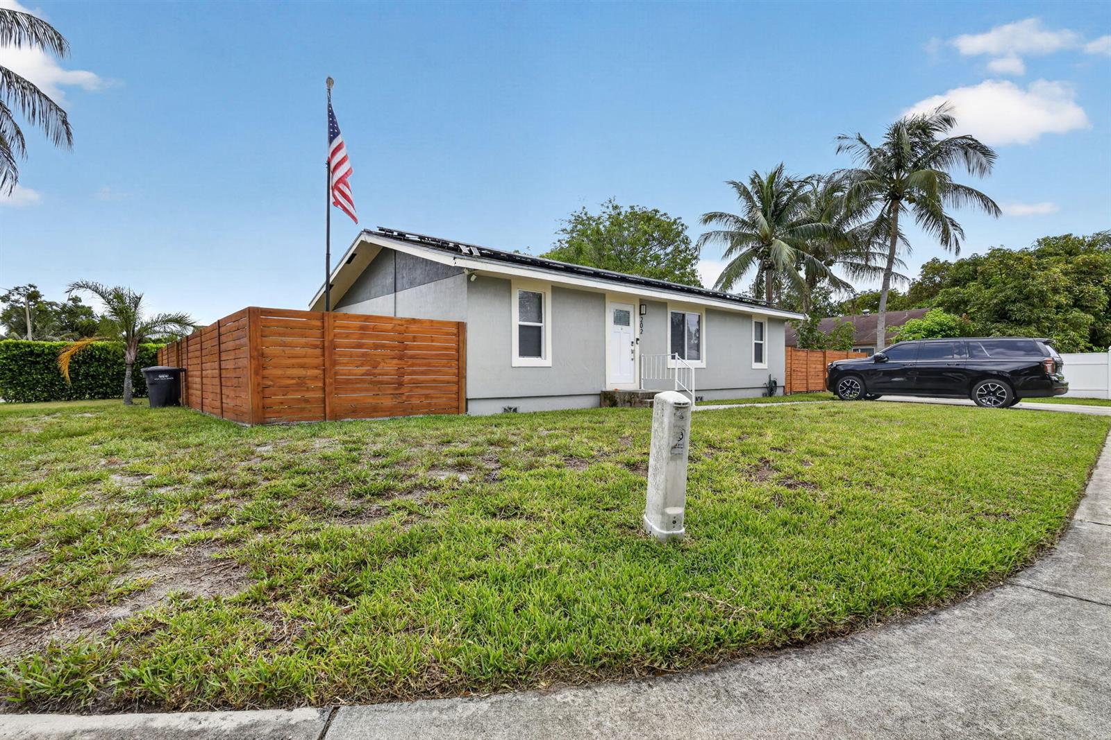 A single-story gray house with a wooden fence, American flag, and a black SUV parked — 202 Elaine Circle W, West Palm Beach FL 33409, WEST PALM BEACH, FL