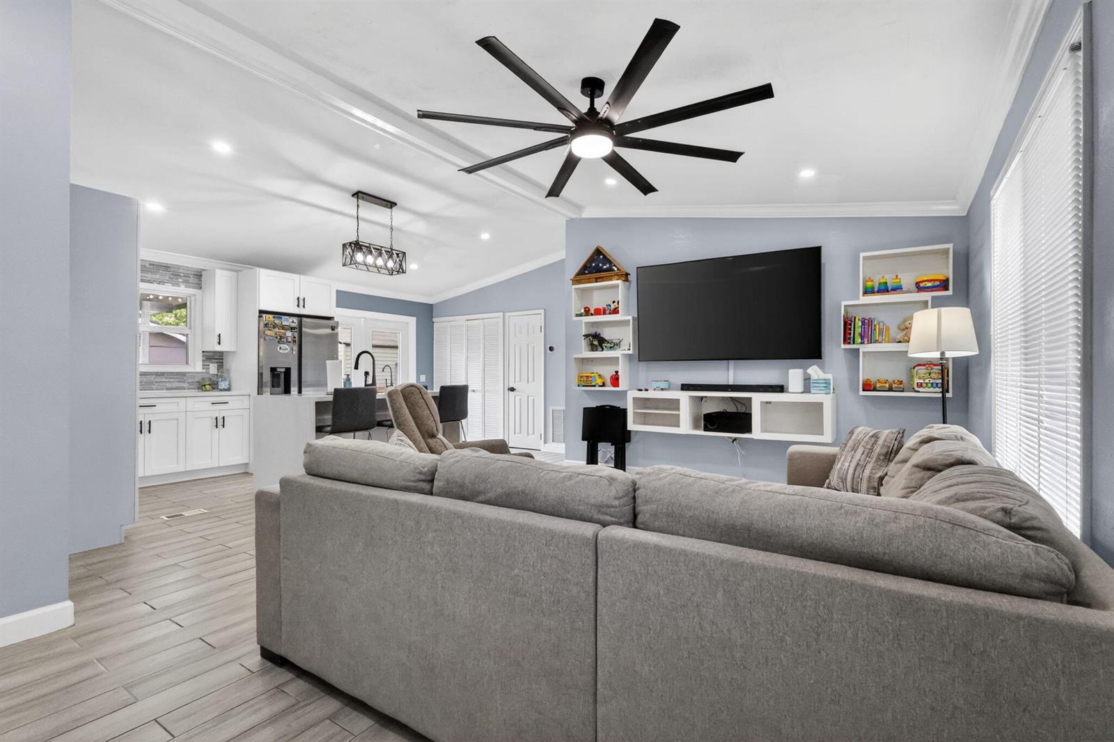 A living room with a gray sectional sofa, a wall-mounted television, and an open kitchen — 202 Elaine Circle W, West Palm Beach FL 33409, WEST PALM BEACH, FL