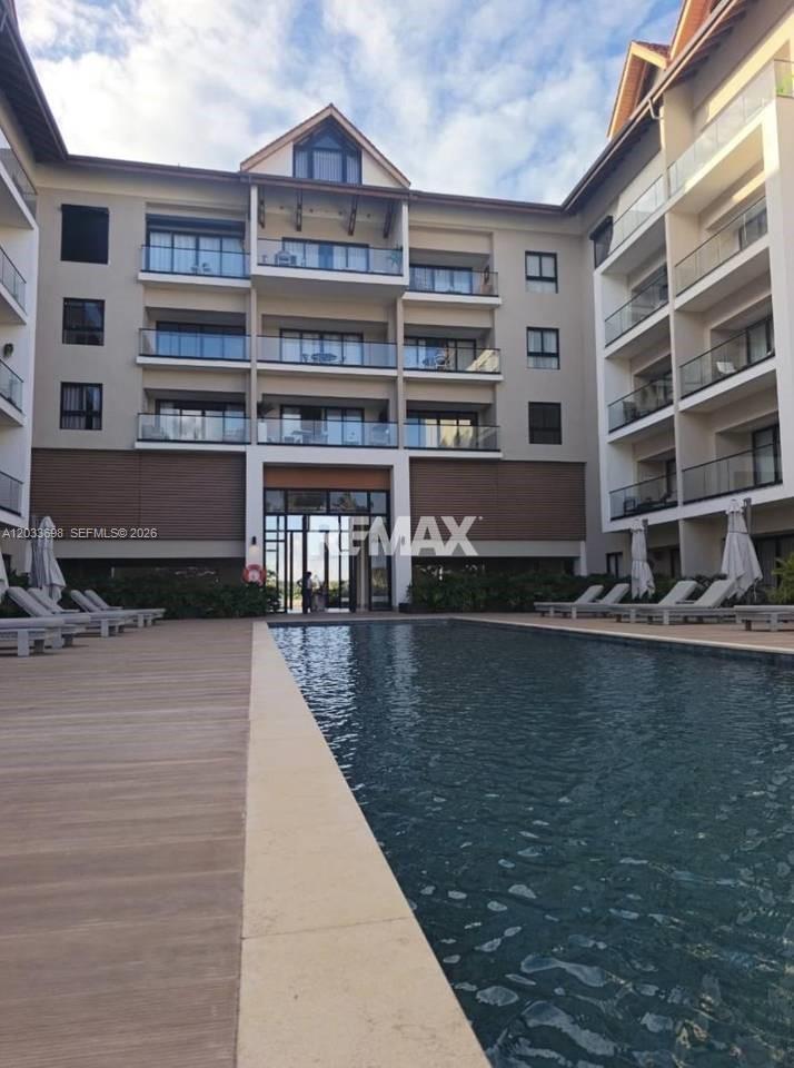 A multi-story apartment building features balconies overlooking a rectangular swimming pool and wooden deck — fh9m Cap Cana # 515, 1 1, 1