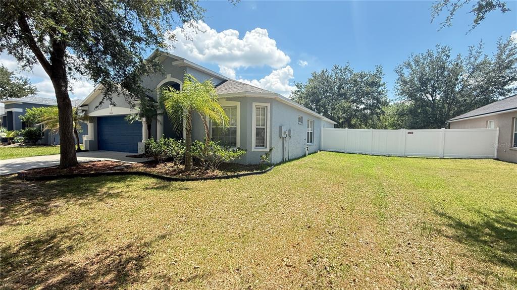 A single-story house with a blue garage, a palm tree, and a white privacy fence — 13464 FLADGATE MARK DRIVE, RIVERVIEW, FL