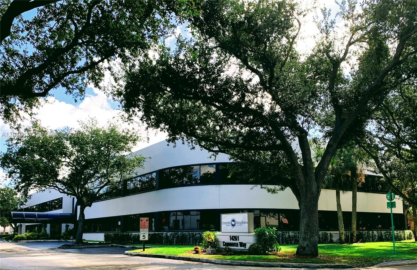 A two-story commercial office building is surrounded by large trees and a paved parking lot — 14261 Commerce Way, Miami Lakes FL 33016, MIAMI LAKES, FL