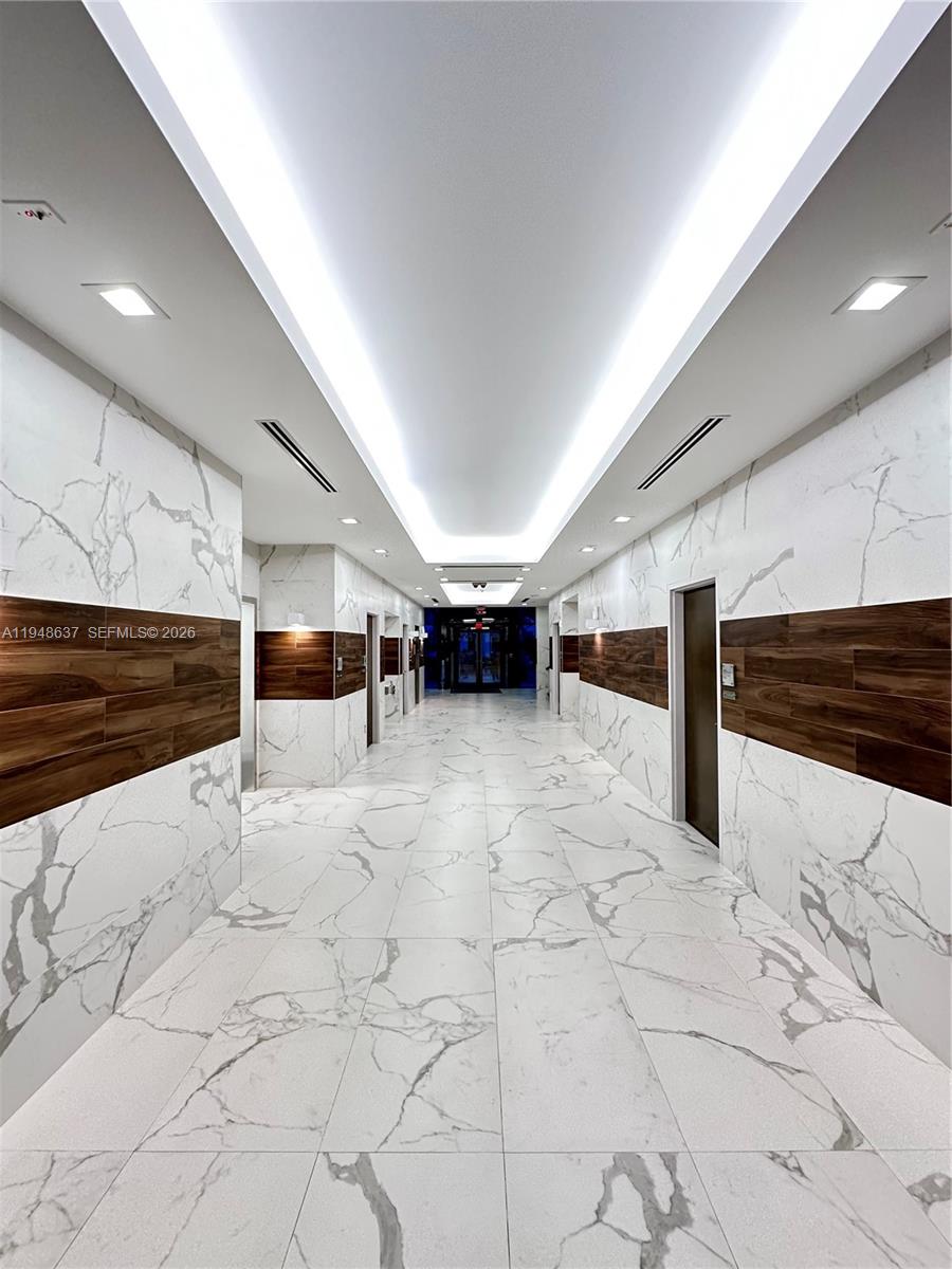 A modern hallway features white marble walls and flooring accented by horizontal wood paneling — 14261 Commerce Way, Miami Lakes FL 33016, MIAMI LAKES, FL