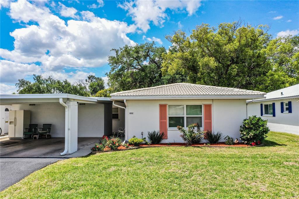 A single-story house with a carport sits between two neighboring homes under a sunset sky — 652 COTTAGE LANE, LAKELAND, FL