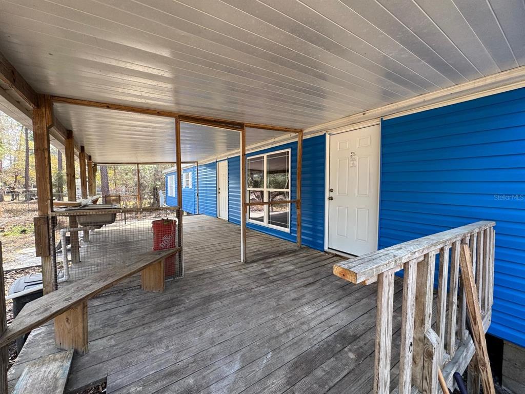 A covered wooden deck features a blue-sided exterior wall, a white door, and railings — 13395 NE 65TH COURT, CITRA, FL