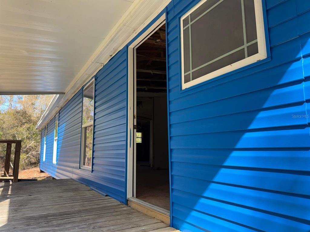 A wooden porch leads to an open doorway on the side of a blue-sided house — 13395 NE 65TH COURT, CITRA, FL