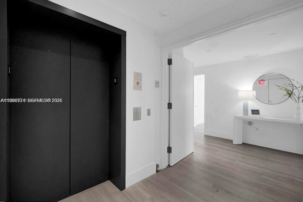 A hallway features a black elevator door, white walls, light wood flooring, and a console table — 788 NE 23rd St # 1402, Miami FL 33137, MIAMI, FL