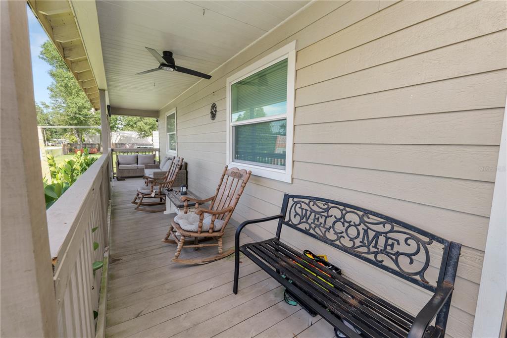 A covered wooden porch features a black metal welcome bench, two rocking chairs, and a ceiling fan — 2001 W BALL STREET, PLANT CITY, FL