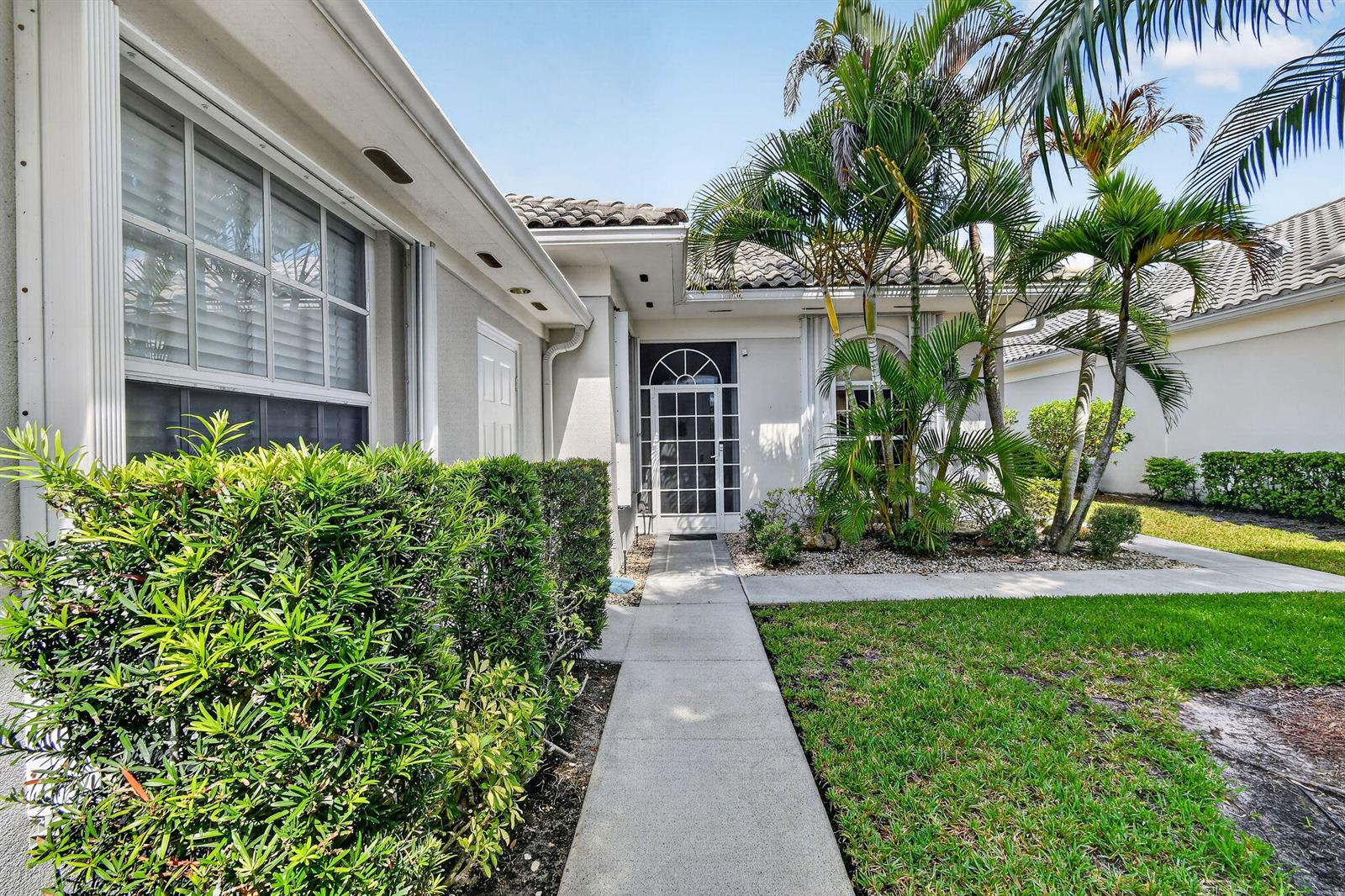 A concrete walkway leads to the front entrance of a house with palm trees — 8081 SE Double Tree Drive, Hobe Sound FL 33455, HOBE SOUND, FL