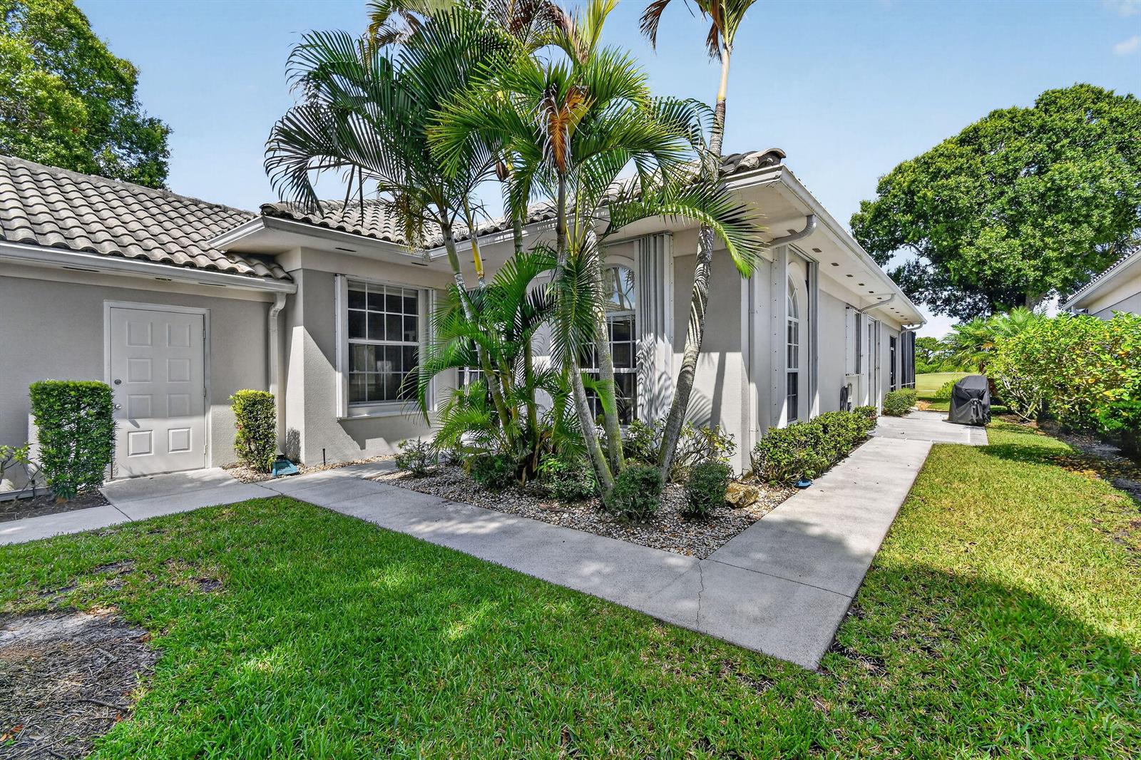 A single-story house exterior features a concrete walkway, palm trees, and a white door — 8081 SE Double Tree Drive, Hobe Sound FL 33455, HOBE SOUND, FL