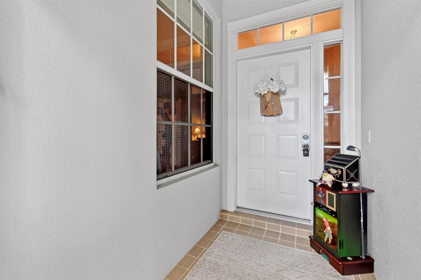 A white front door with a transom window and sidelight sits beside a large window — 8081 SE Double Tree Drive, Hobe Sound FL 33455, HOBE SOUND, FL