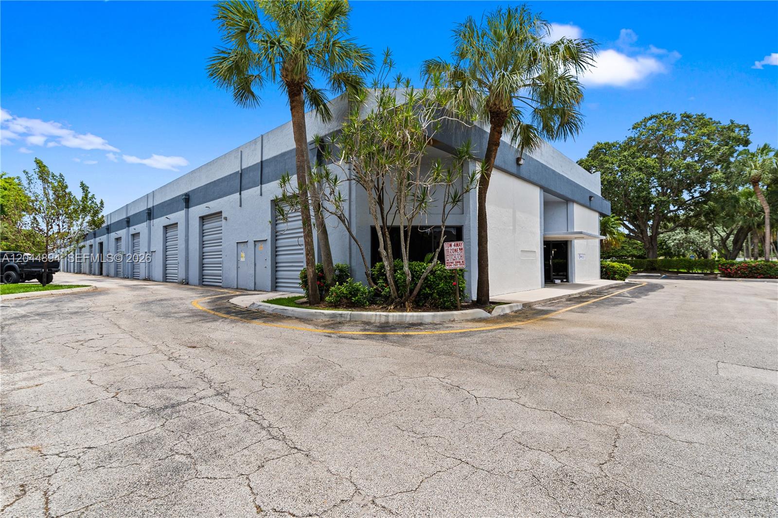A low-rise industrial building features multiple roll-up doors, a corner entrance, and palm trees — 10297 NW 46th St # 1A, Sunrise FL 33351, SUNRISE, FL