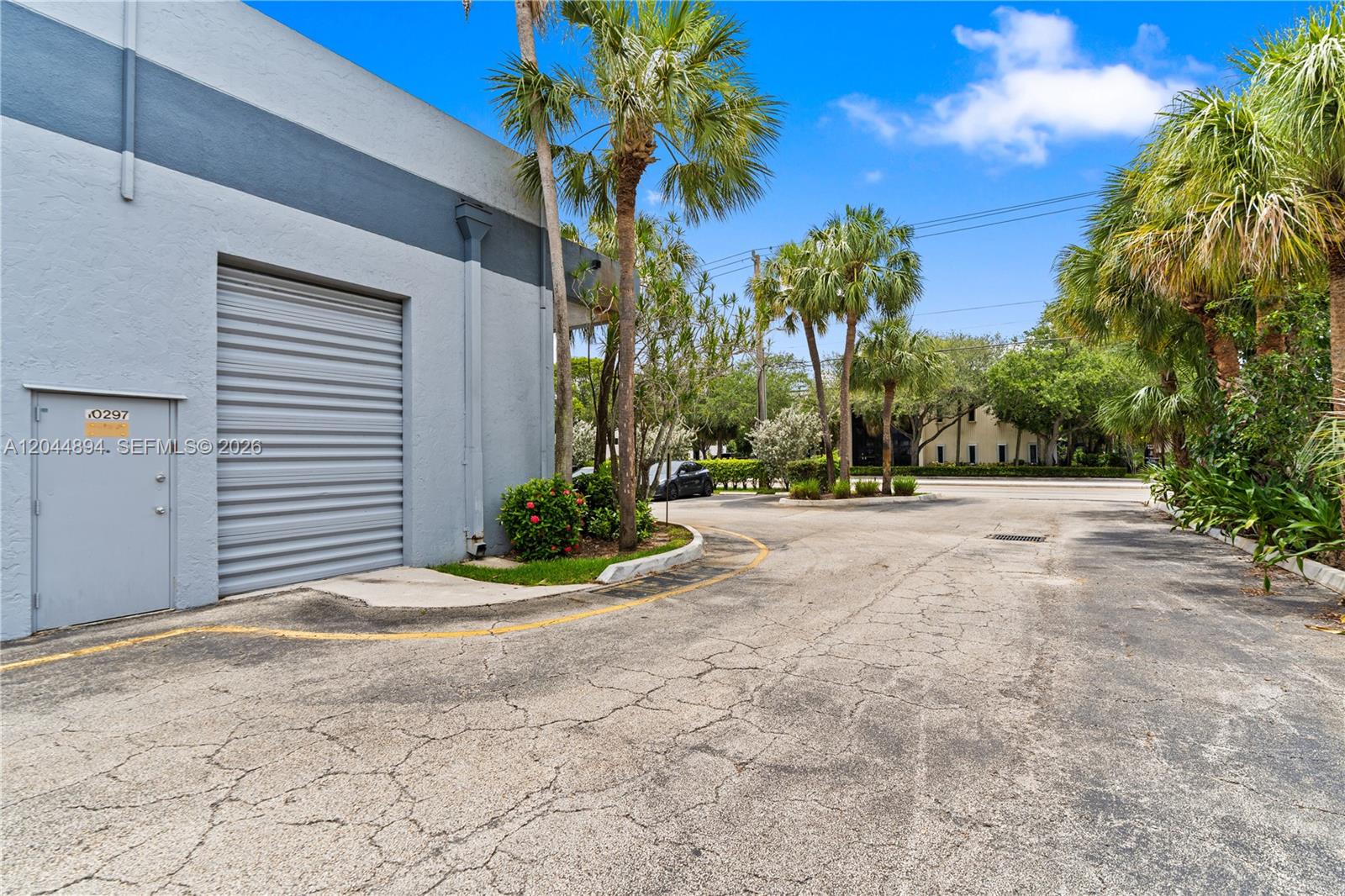 An exterior view shows a gray industrial building with a roll-up door and palm trees — 10297 NW 46th St # 1A, Sunrise FL 33351, SUNRISE, FL