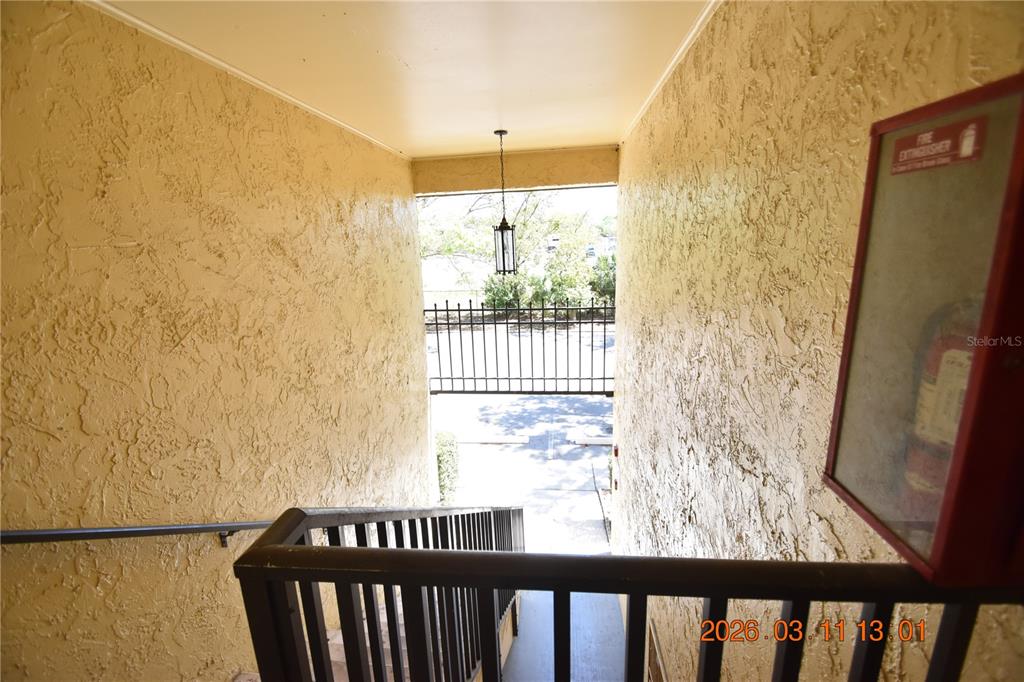 An outdoor stairwell with textured walls, a dark railing, and a wall-mounted fire extinguisher cabinet — 3910 44TH STREET N UNIT C9, ST PETERSBURG, FL