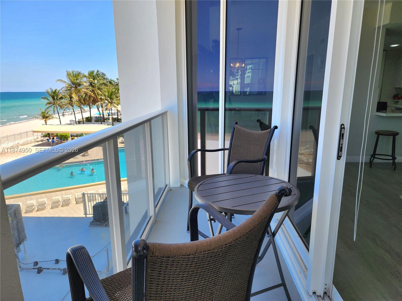 A balcony with a small table and two chairs overlooks a swimming pool and beach — 3505 S Ocean Dr # 312, Hollywood FL 33019, HOLLYWOOD, FL