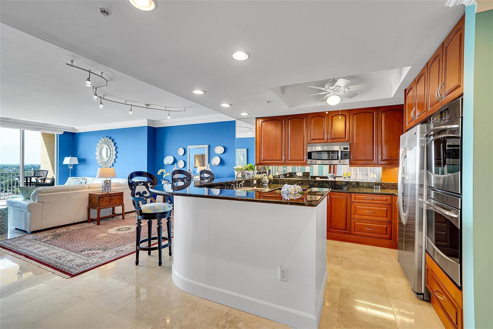 A kitchen with wood cabinets and granite countertops opens to a living room with blue walls — 821 N Riverside Drive, Pompano Beach FL 33062, POMPANO BEACH, FL