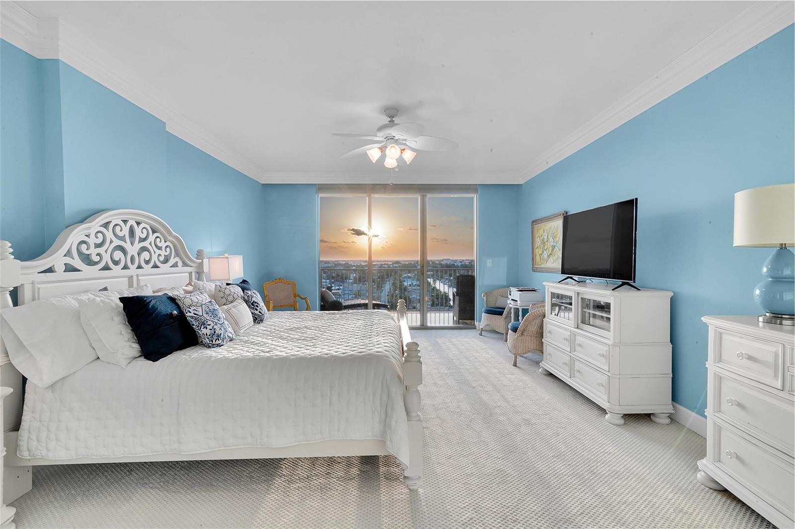 A bedroom with light blue walls, a white bed frame, and a balcony overlooking sunset — 821 N Riverside Drive, Pompano Beach FL 33062, POMPANO BEACH, FL