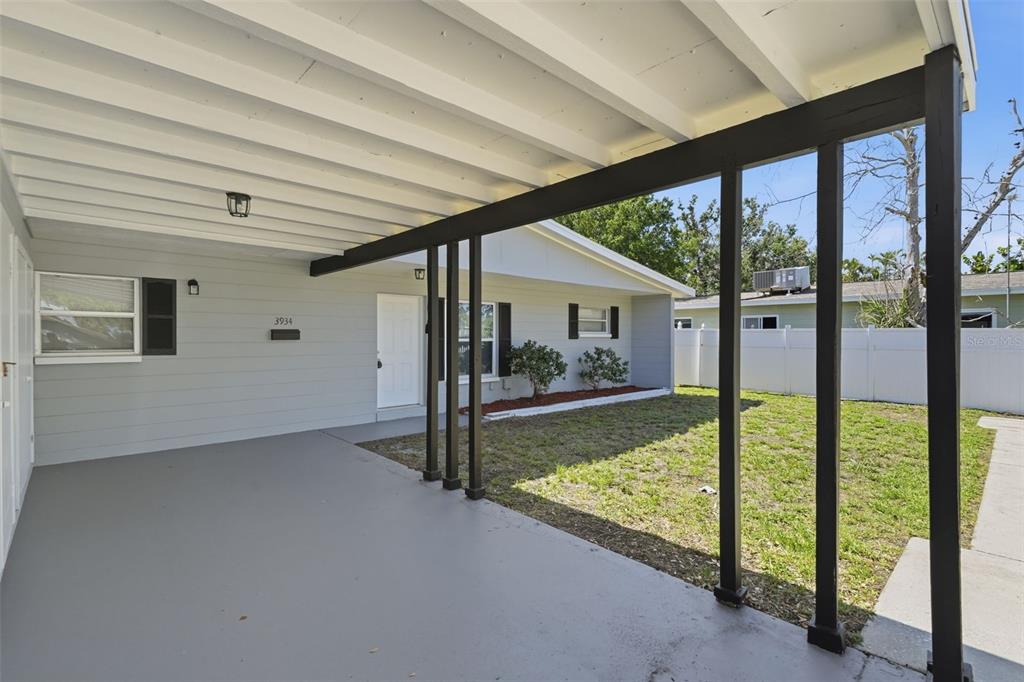 A covered patio with a gray concrete floor overlooks a grassy yard and house exterior — 3934 HELENA STREET NE, ST PETERSBURG, FL