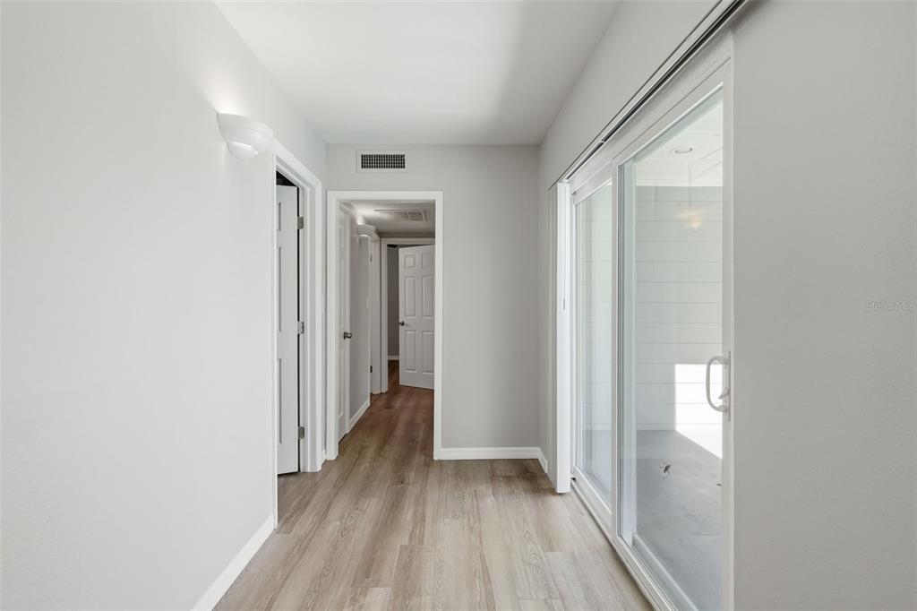 A hallway with light wood-look flooring leads to a doorway and a sliding glass door — 3934 HELENA STREET NE, ST PETERSBURG, FL