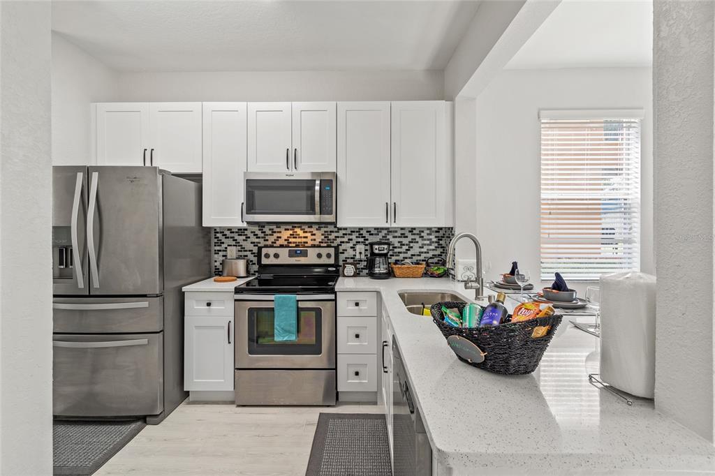 A kitchen features white cabinets, stainless steel appliances, a mosaic backsplash, and a quartz countertop — 4040 CALABRIA AVENUE, DAVENPORT, FL