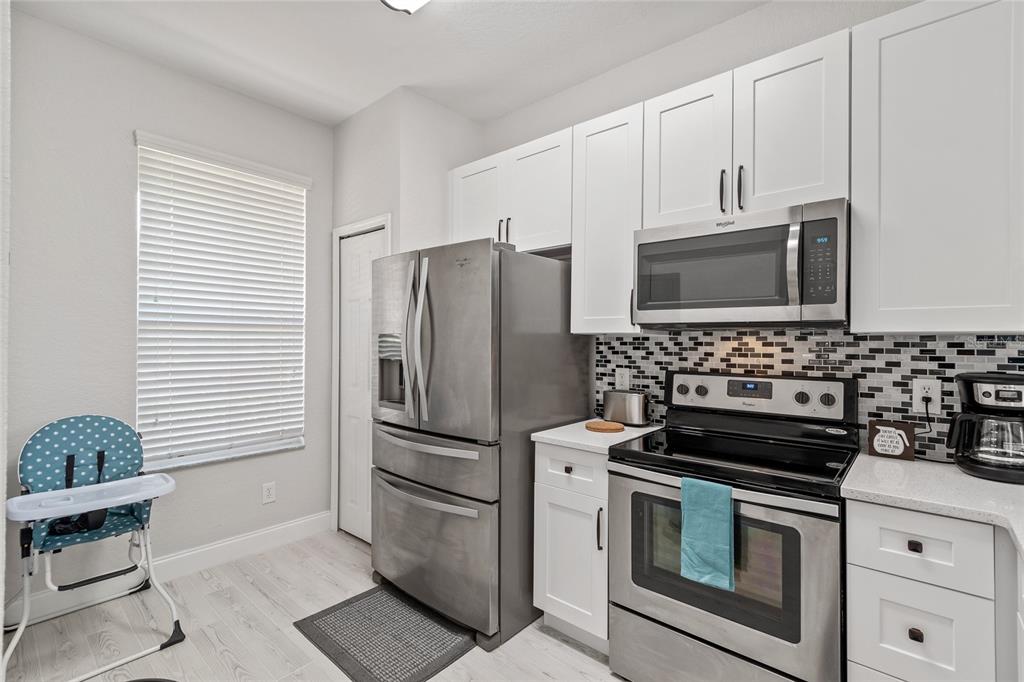 A kitchen features white cabinets, stainless steel appliances, a mosaic backsplash, and a high chair — 4040 CALABRIA AVENUE, DAVENPORT, FL