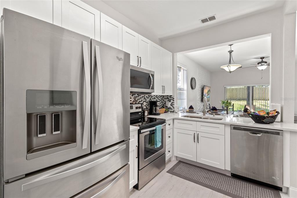 A modern kitchen features white cabinets, stainless steel appliances, and a view into the dining area — 4040 CALABRIA AVENUE, DAVENPORT, FL