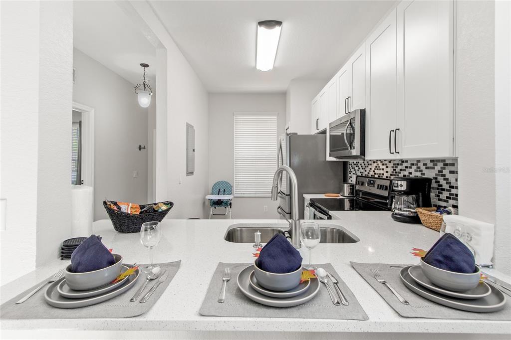 A kitchen with white cabinets, stainless steel appliances, and a breakfast bar with three place settings — 4040 CALABRIA AVENUE, DAVENPORT, FL