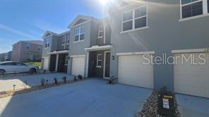A row of multi-story townhouses with attached garages and a concrete driveway under a blue sky — 1215 DRAINTREE STREET, DAVENPORT, FL