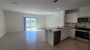 An open-concept kitchen with white cabinets and an island overlooks a living area with tile — 1215 DRAINTREE STREET, DAVENPORT, FL