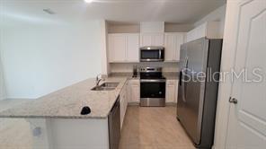 A kitchen features white cabinets, granite countertops, a kitchen island, and stainless steel appliances — 1215 DRAINTREE STREET, DAVENPORT, FL