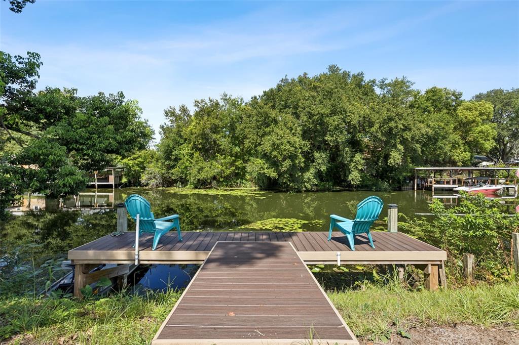 A wooden dock with two blue Adirondack chairs overlooks a calm, tree-lined canal — 27821 LOIS DRIVE, TAVARES, FL
