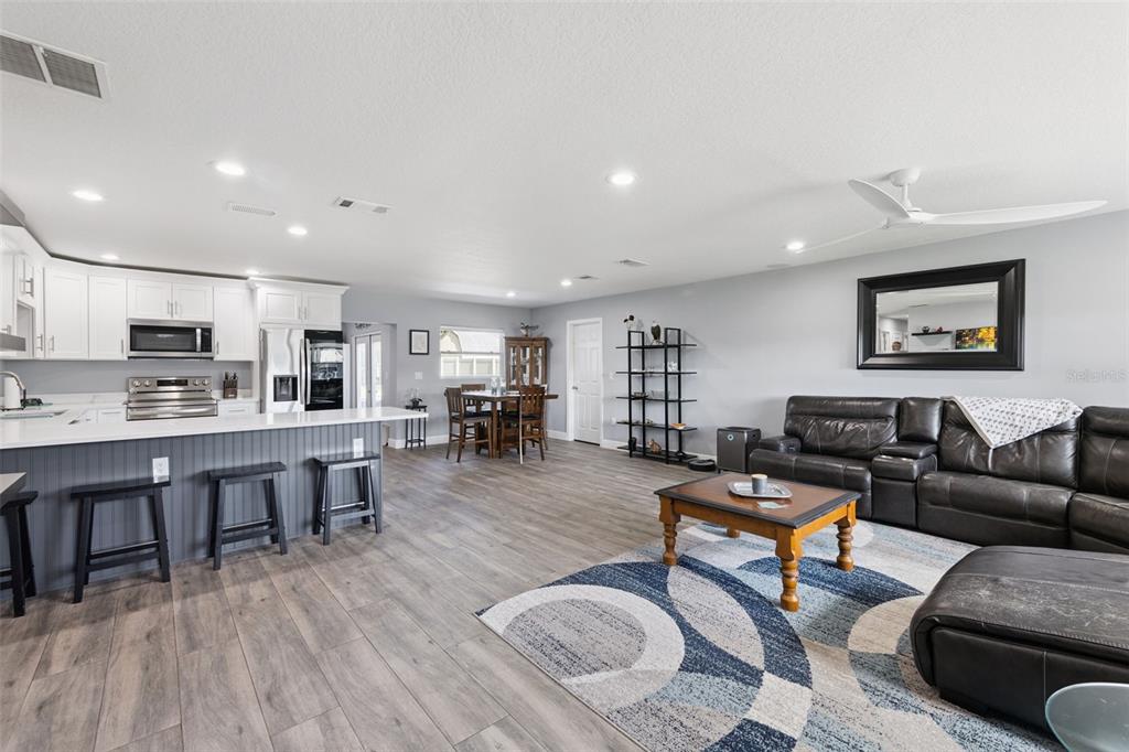 An open-concept living room and kitchen featuring white cabinets, a gray island, and wood-look flooring — 27821 LOIS DRIVE, TAVARES, FL