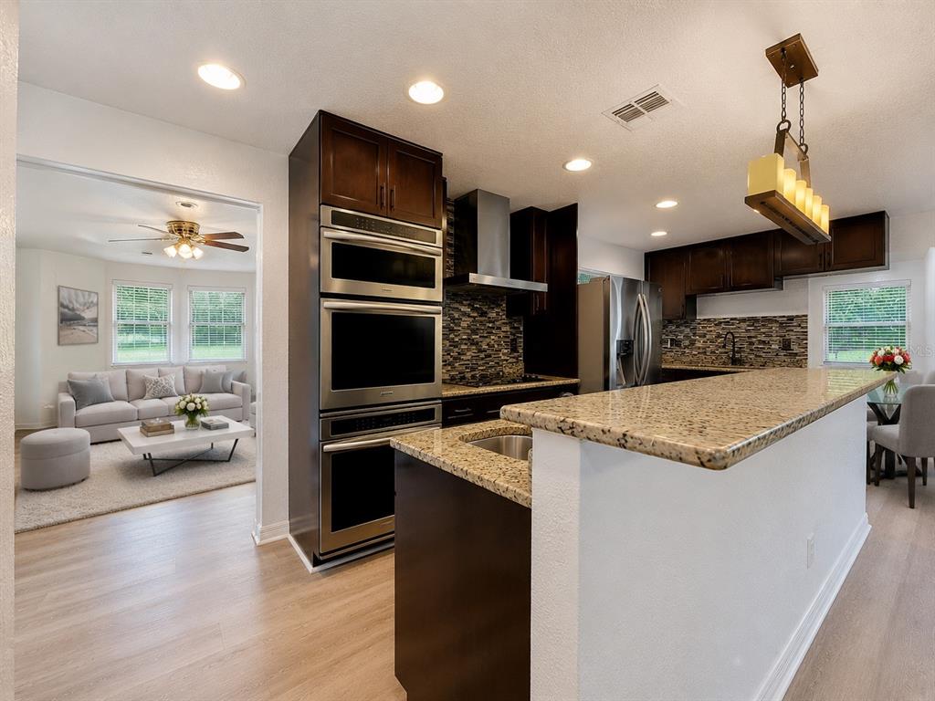 A kitchen with dark wood cabinets, granite countertops, and stainless steel appliances overlooks a living room — 1926 MEADOWRIDGE DRIVE, VALRICO, FL