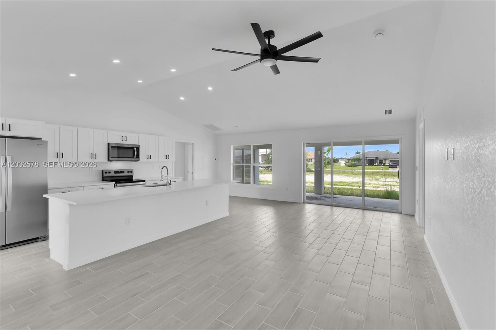 A modern kitchen with white cabinetry and an island opens to a bright living area — 4130 NW 33rd, Cape Coral FL 33993, CAPE CORAL, FL