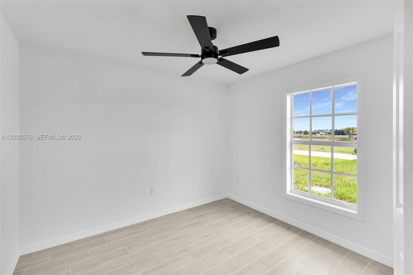 A bright, empty room features white walls, light tile flooring, and a black ceiling fan — 4130 NW 33rd, Cape Coral FL 33993, CAPE CORAL, FL