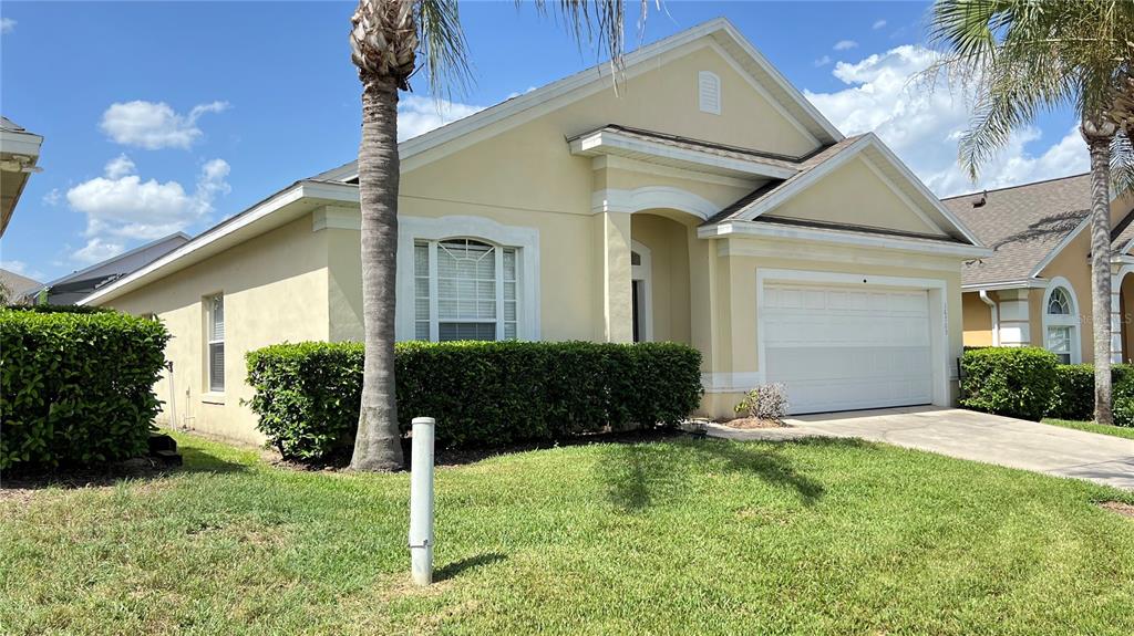 A single-story house with a beige stucco exterior, a two-car garage, and a palm tree — 16709 FRESH MEADOW DRIVE, CLERMONT, FL