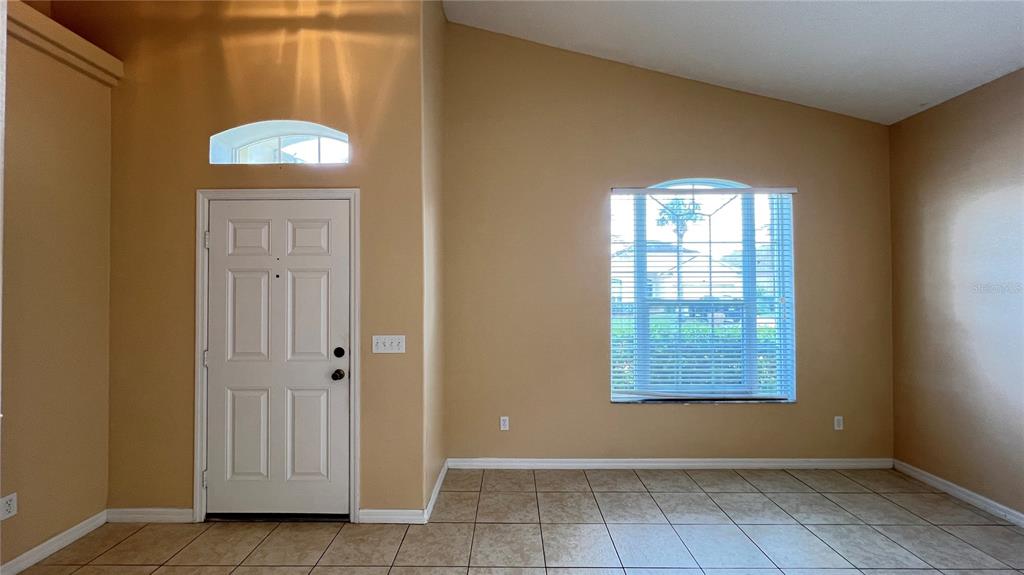 An empty room features tan walls, tile flooring, a white front door, and a window — 16709 FRESH MEADOW DRIVE, CLERMONT, FL