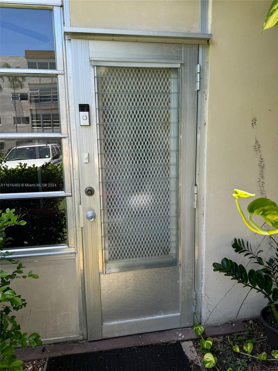 A silver metal security door with a diamond-patterned screen sits beside a large window — 4047 NW 16th St # 110, Lauderhill FL 33313, LAUDERHILL, FL