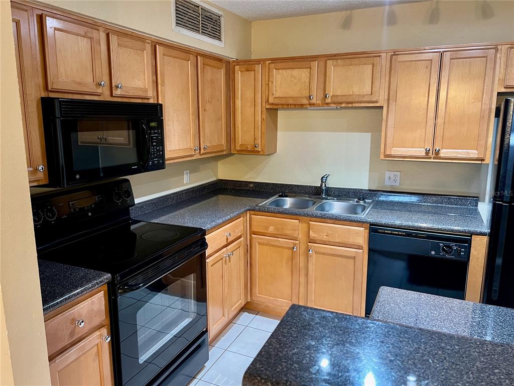 An open-concept living room with a fireplace, ceiling fan, and an adjacent kitchen with cabinets — 375 LAKE ONTARIO COURT UNIT 203, ALTAMONTE SPRINGS, FL