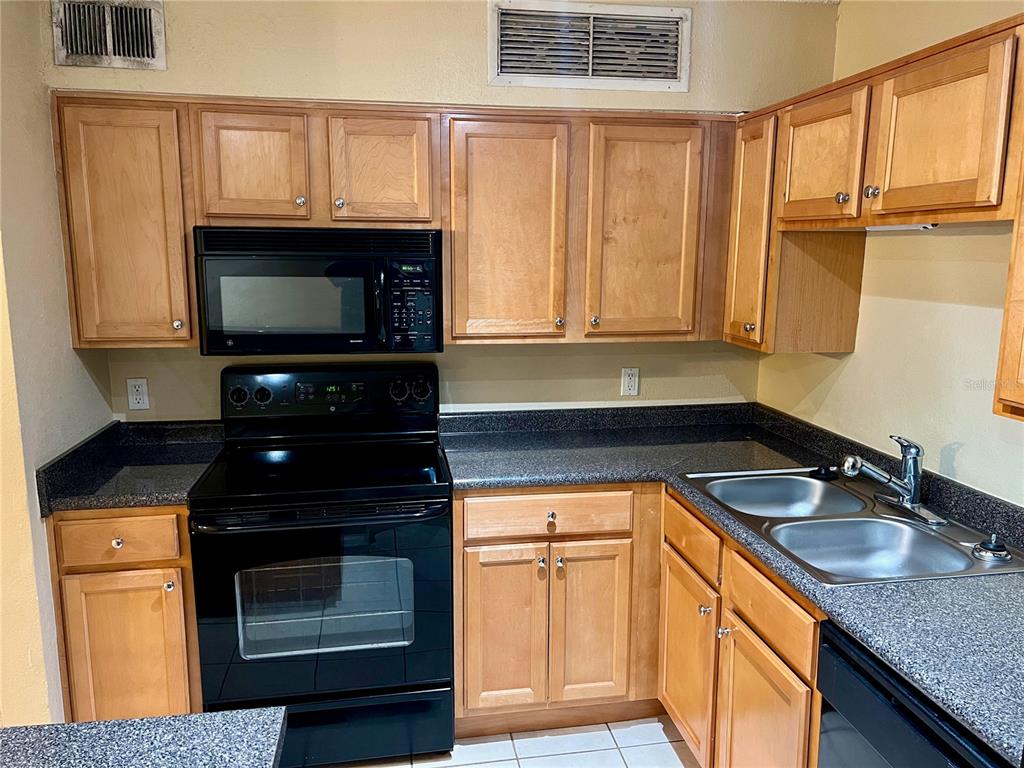 A kitchen features wood cabinets, dark granite countertops, stainless steel appliances, and a breakfast bar — 375 LAKE ONTARIO COURT UNIT 203, ALTAMONTE SPRINGS, FL