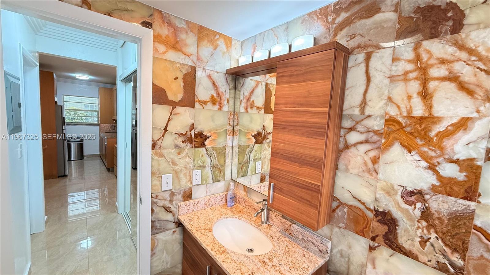 A bathroom features a wood vanity, a vessel sink, and walls covered in marble tiles — 650 Pennsylvania Ave # 2, Miami Beach FL 33139, MIAMI BEACH, FL