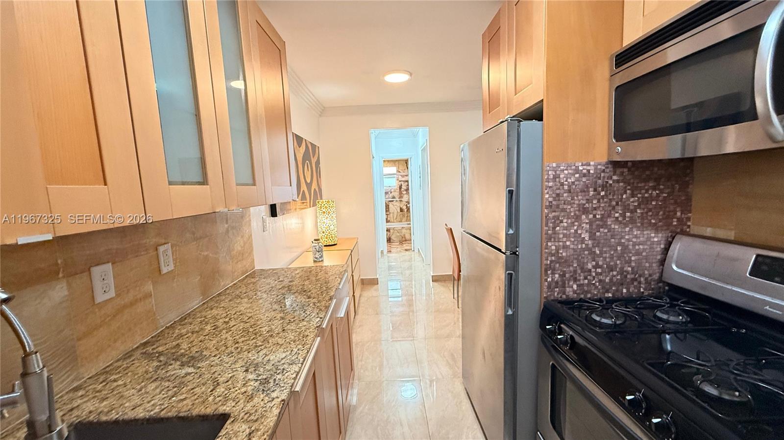 A galley kitchen features light wood cabinets, granite countertops, and stainless steel appliances — 650 Pennsylvania Ave # 2, Miami Beach FL 33139, MIAMI BEACH, FL