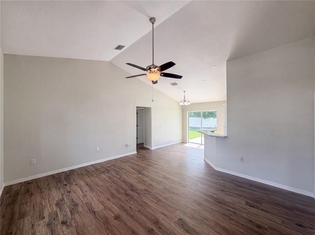 An open-concept living area features vaulted ceilings, a ceiling fan, and wood-look flooring — 5434 PARNELL AVENUE, SPRING HILL, FL