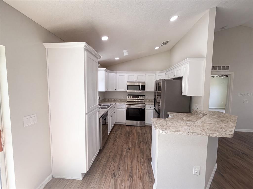 A kitchen features white cabinetry, stainless steel appliances, and a peninsula with stone-look countertops — 5434 PARNELL AVENUE, SPRING HILL, FL