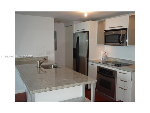 A modern kitchen features a granite-topped island, stainless steel appliances, and white cabinetry — 185 SW 7th St # 1909, Miami FL 33130, MIAMI, FL