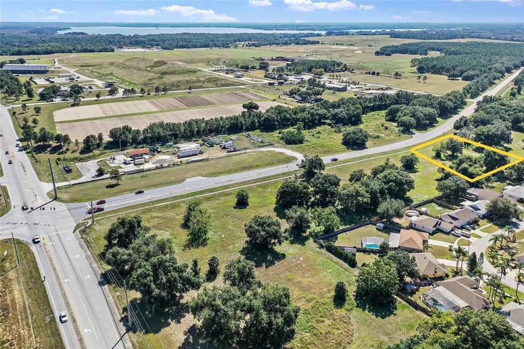 An aerial view shows a vacant, tree-covered lot outlined in yellow near a road intersection — CR-448 Lot 4, TAVARES, FL